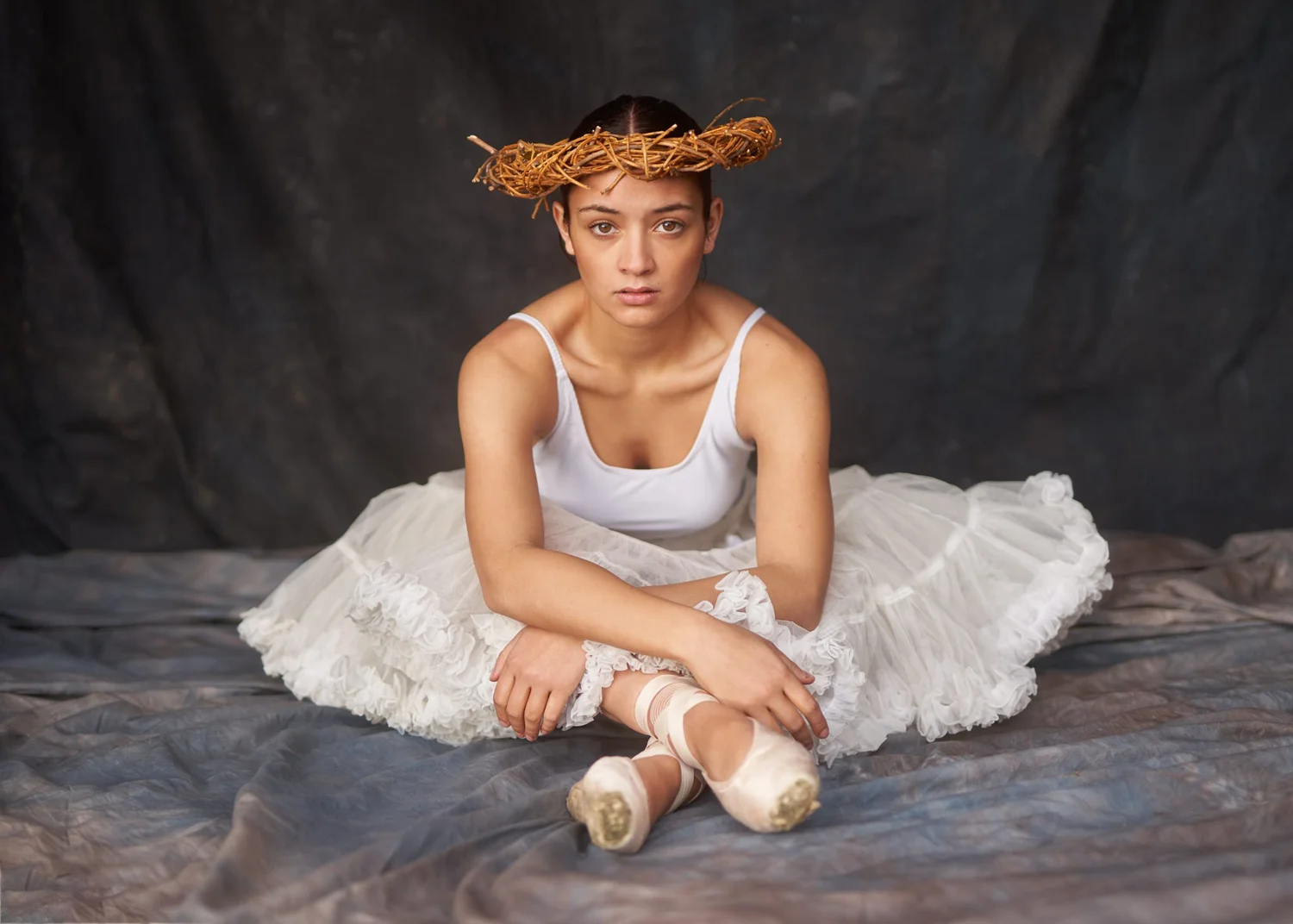 A ballerina in a white tutu and floral crown sitting on the floor