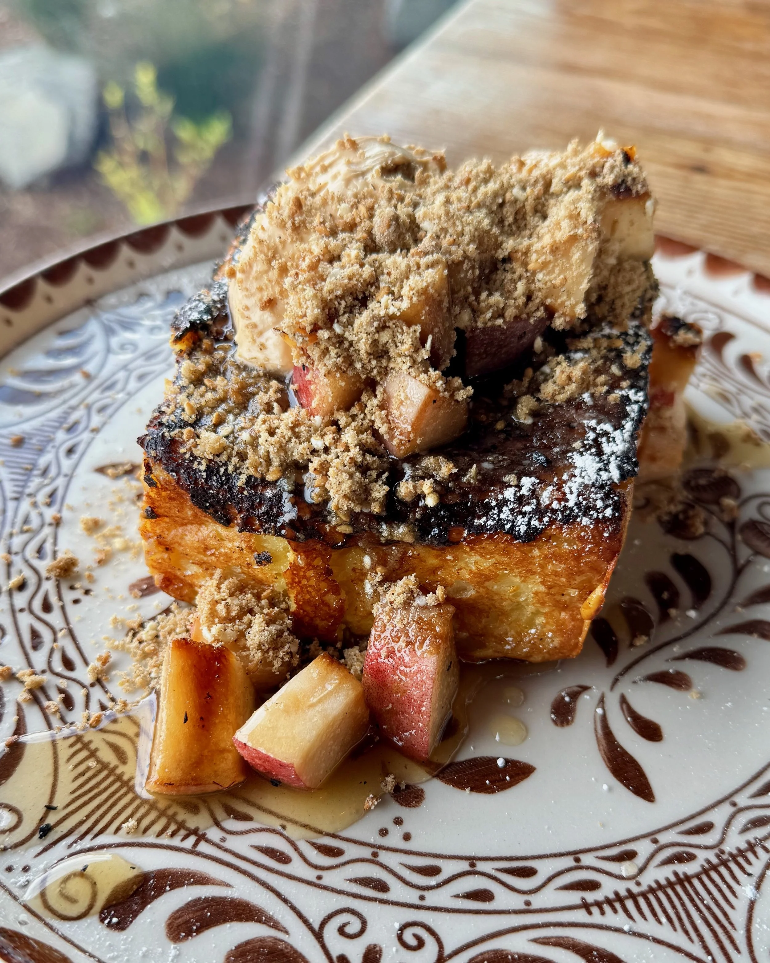 A slice of our decadent french toast, served on a decorative plate with maple syrup and dusted with powdered sugar.