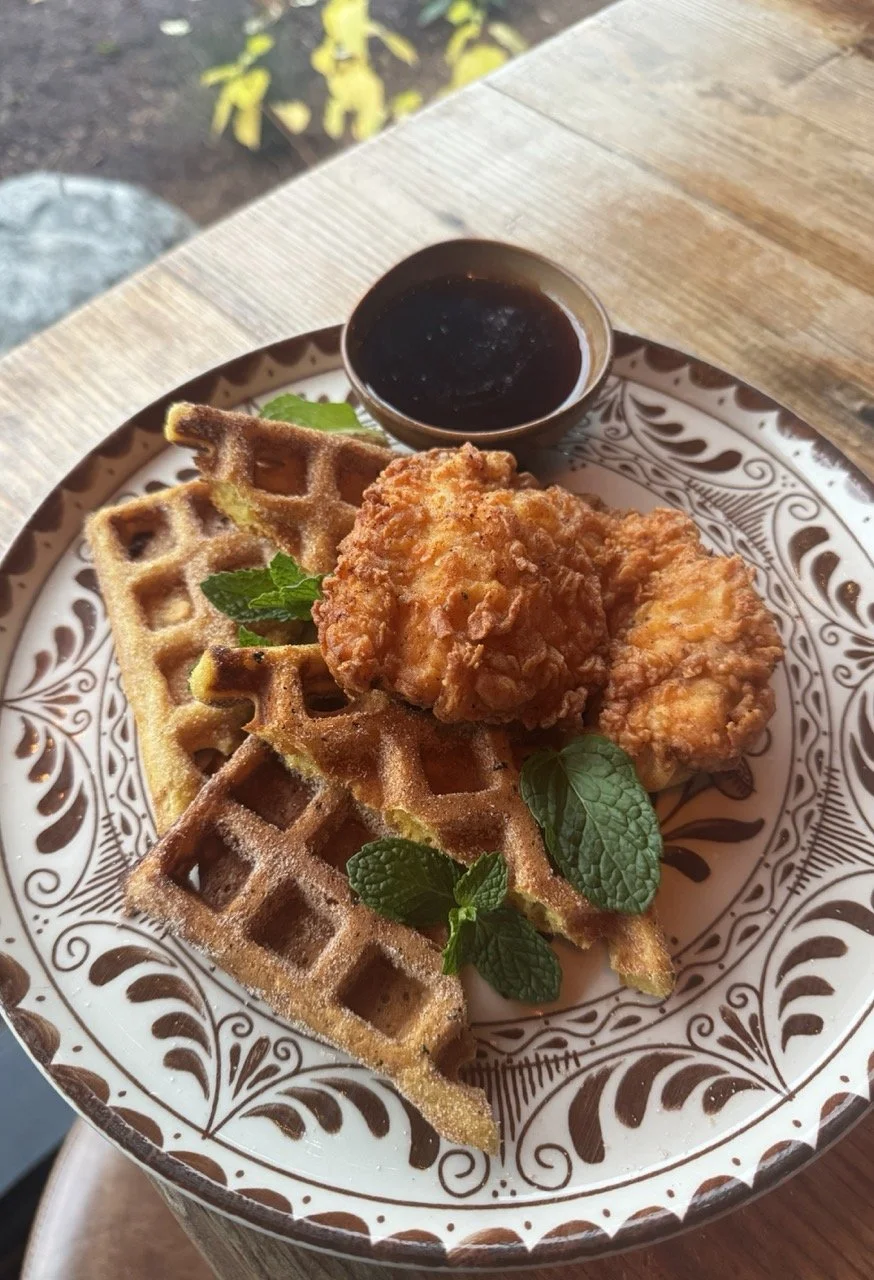 Plate with fried chicken strip, waffles, syrup, and mint leaves, on a decorative plate.