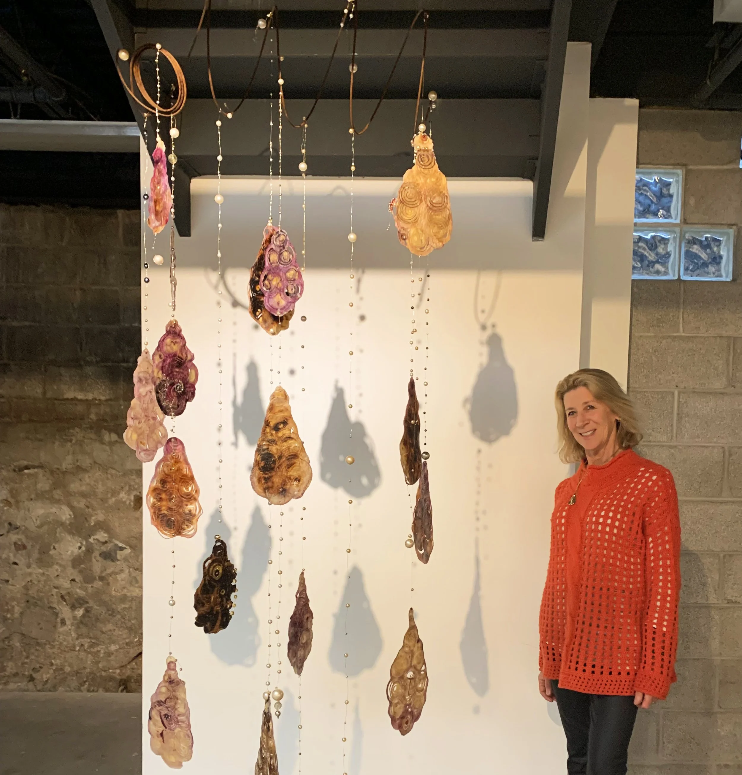 Nanci Hersh standing beside suspended mixed media installation with organic layered forms and translucent materials, exploring memory, body, and transformation