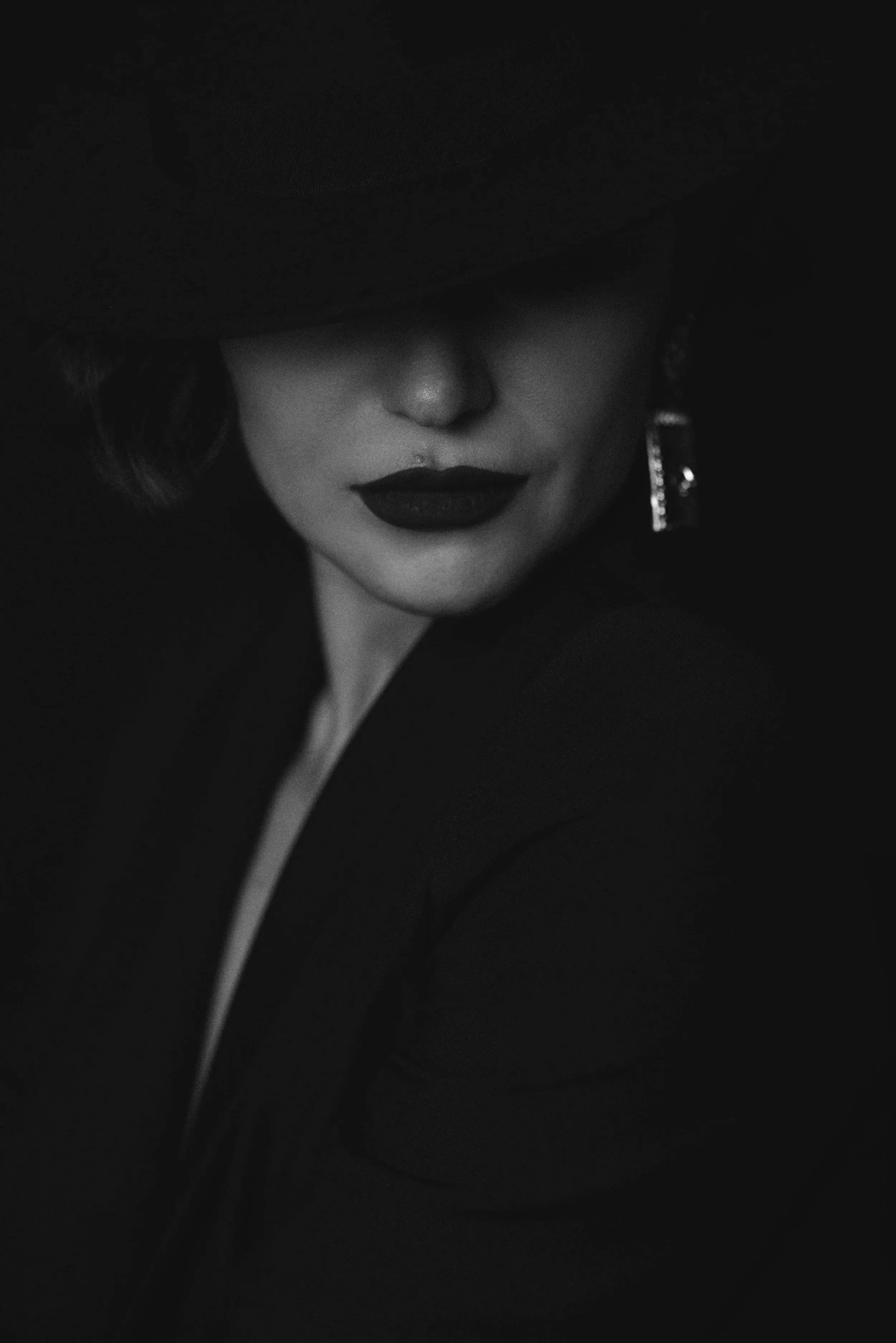 A woman wearing a black hat and lipstick, with her eyes covered by the hat's brim, smiling slightly.