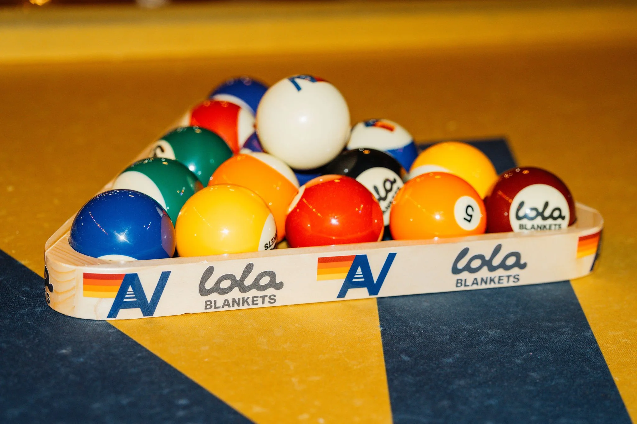 Billiard balls inside a wooden rack on a pool table with yellow and blue felt.