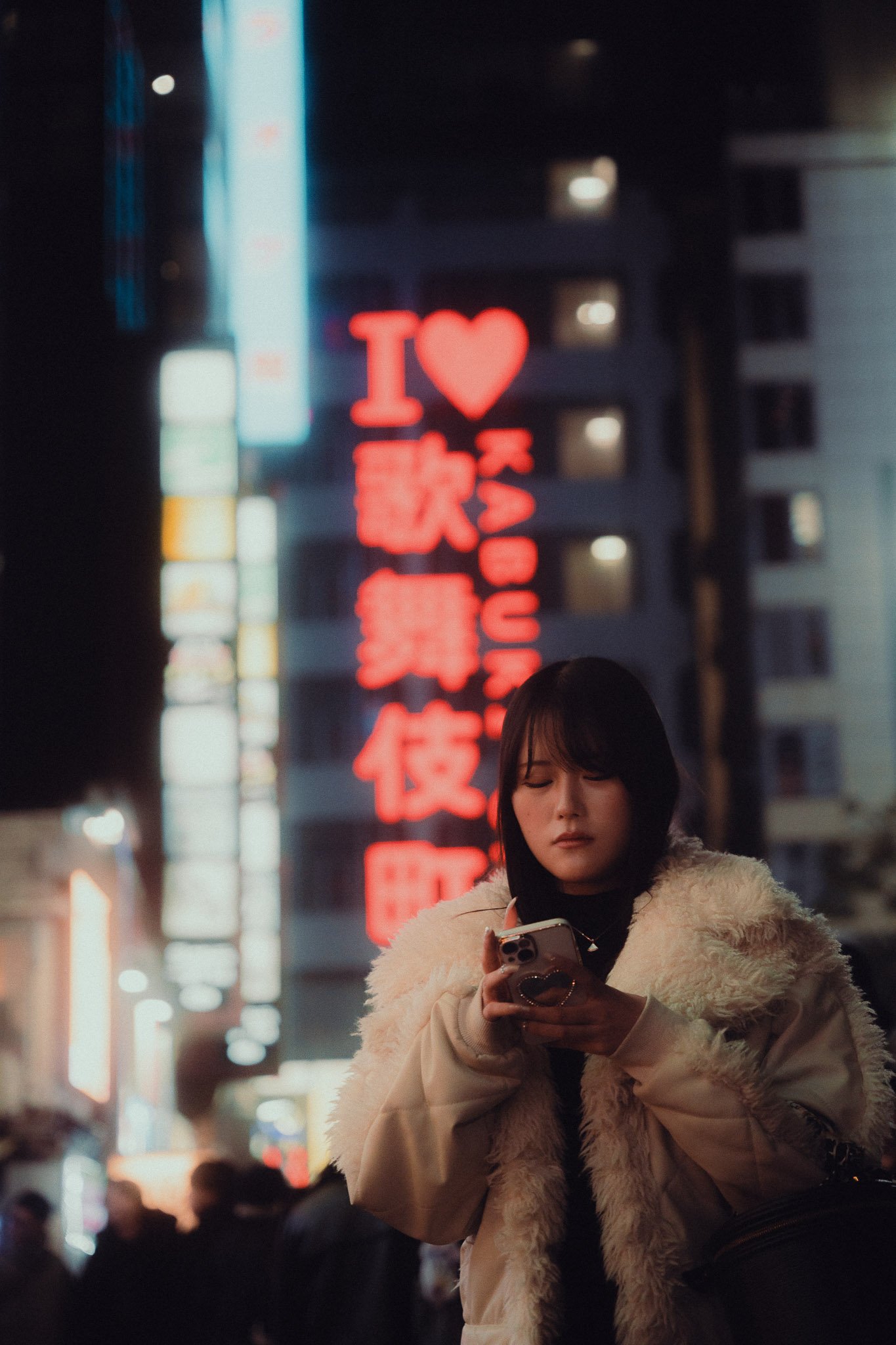 Mujer con abrigo blanco usando un teléfono, luces de neón rojas y azules en el fondo urbano.
