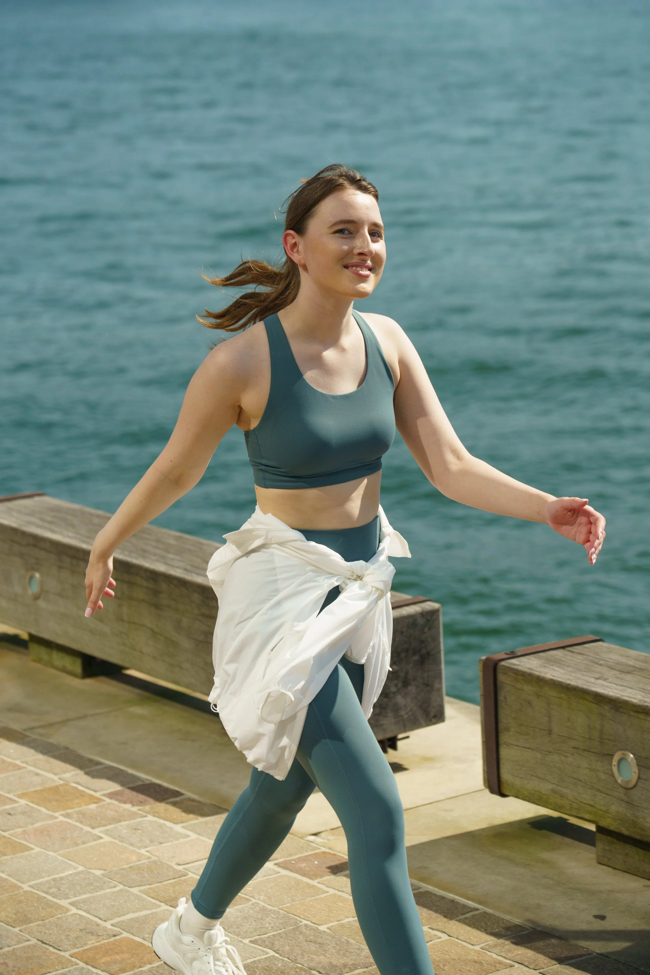 A woman in athletic wear jogging along a waterfront promenade near the ocean.