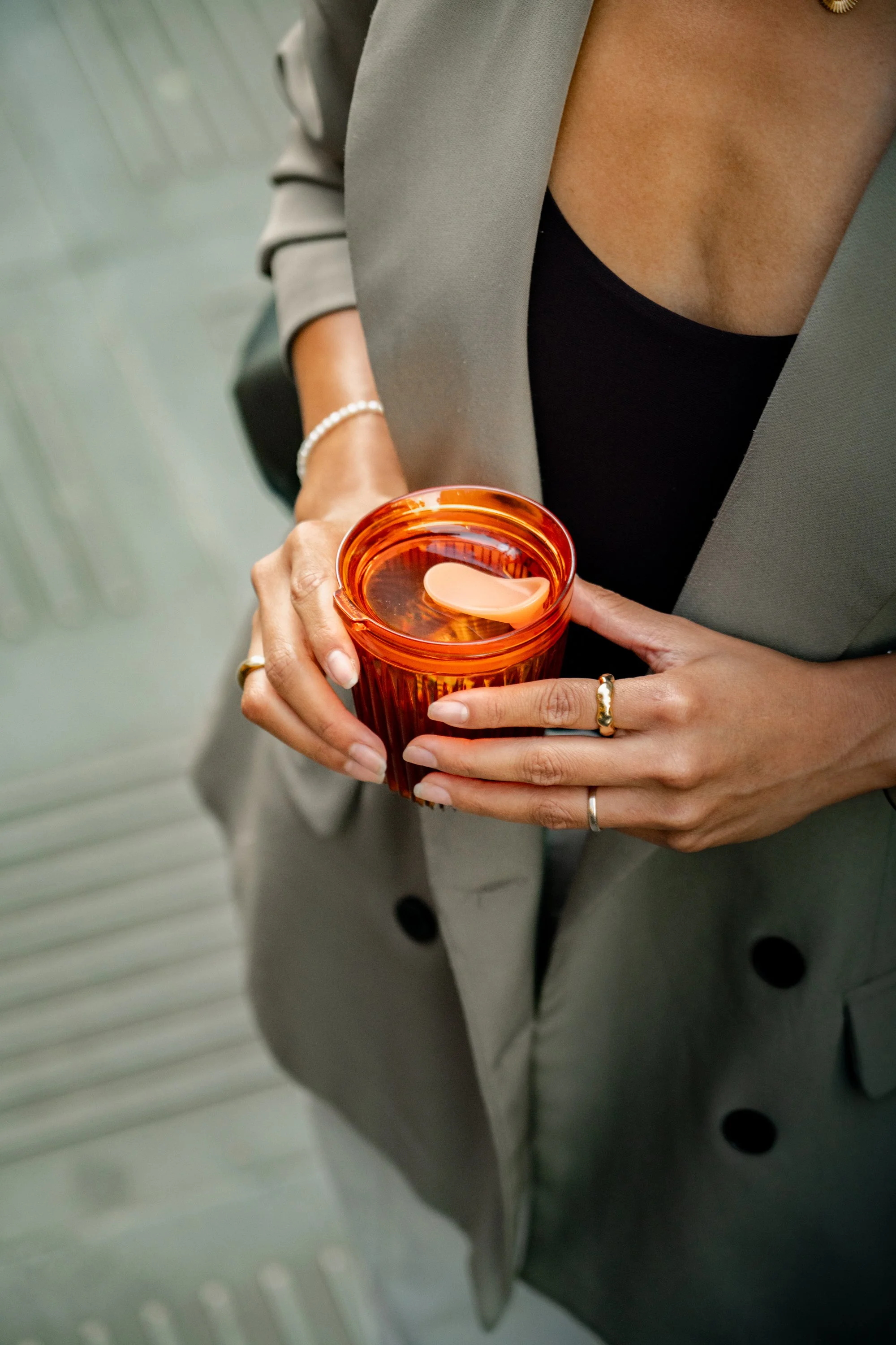 Person wearing a gray blazer and black top holding an orange glass with a spoon inside.