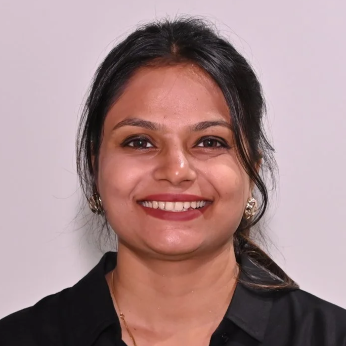 Smiling woman with dark hair, earrings, and a black shirt against a plain background.