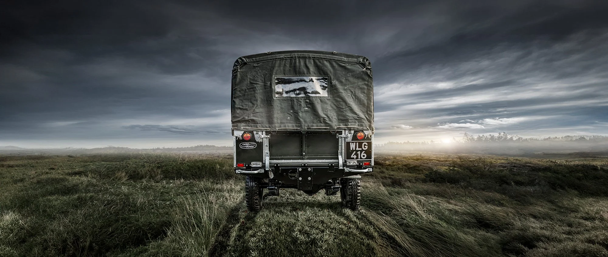 Vintage Land Rover Defender rear view in the middle of a grass field.
