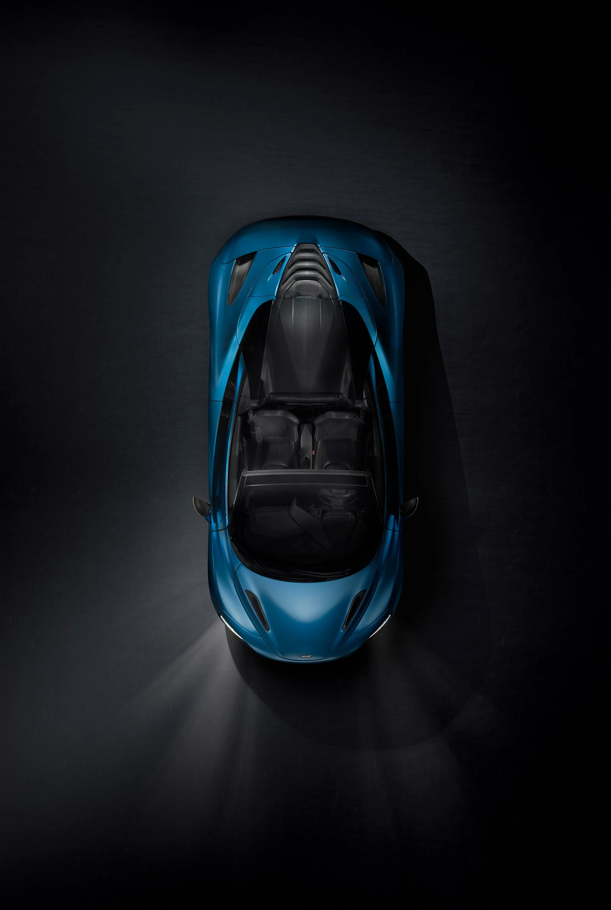 Overhead view of a McLaren car from above with headlights on in dark studio scene.