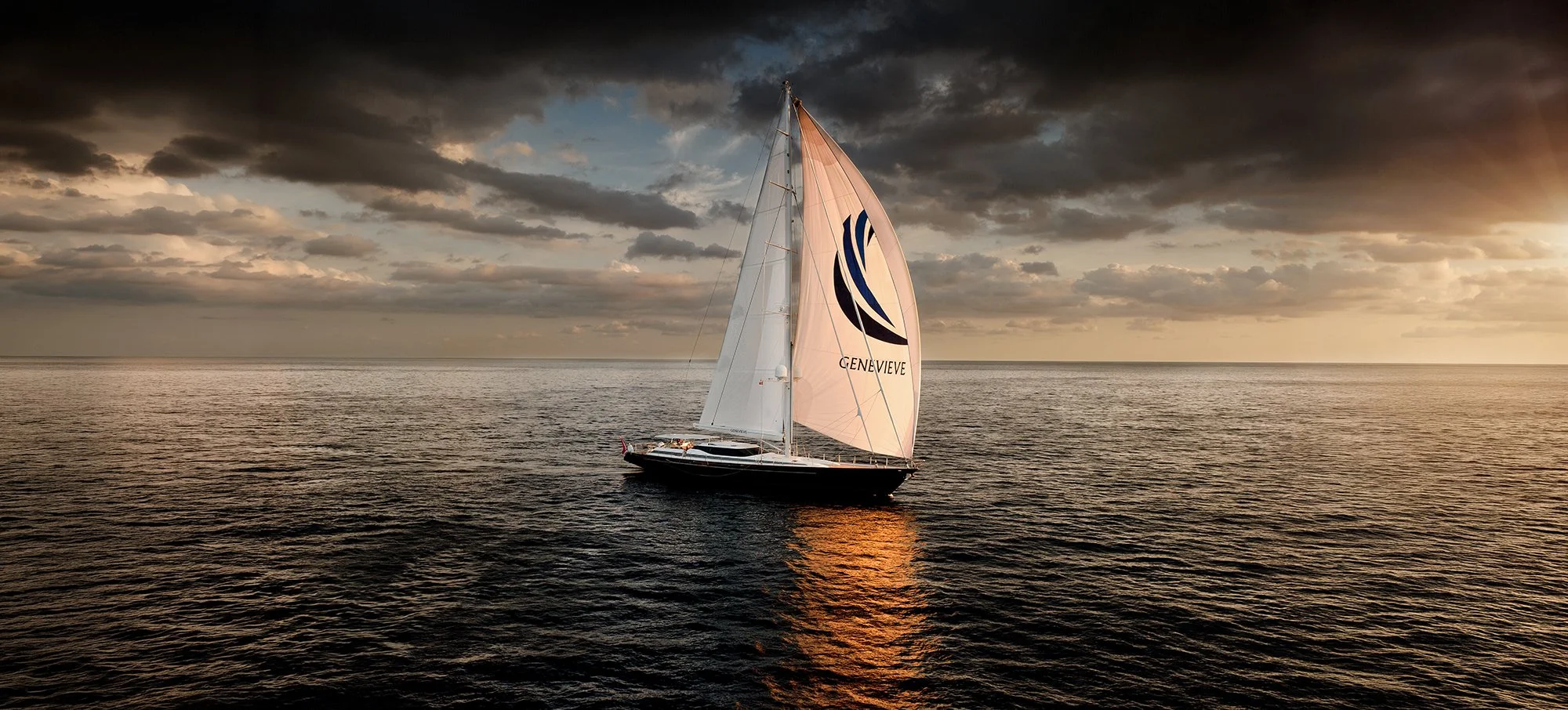 Aerial view from helicopter of luxury super yacht sailing across open water with sun setting in the distance. 