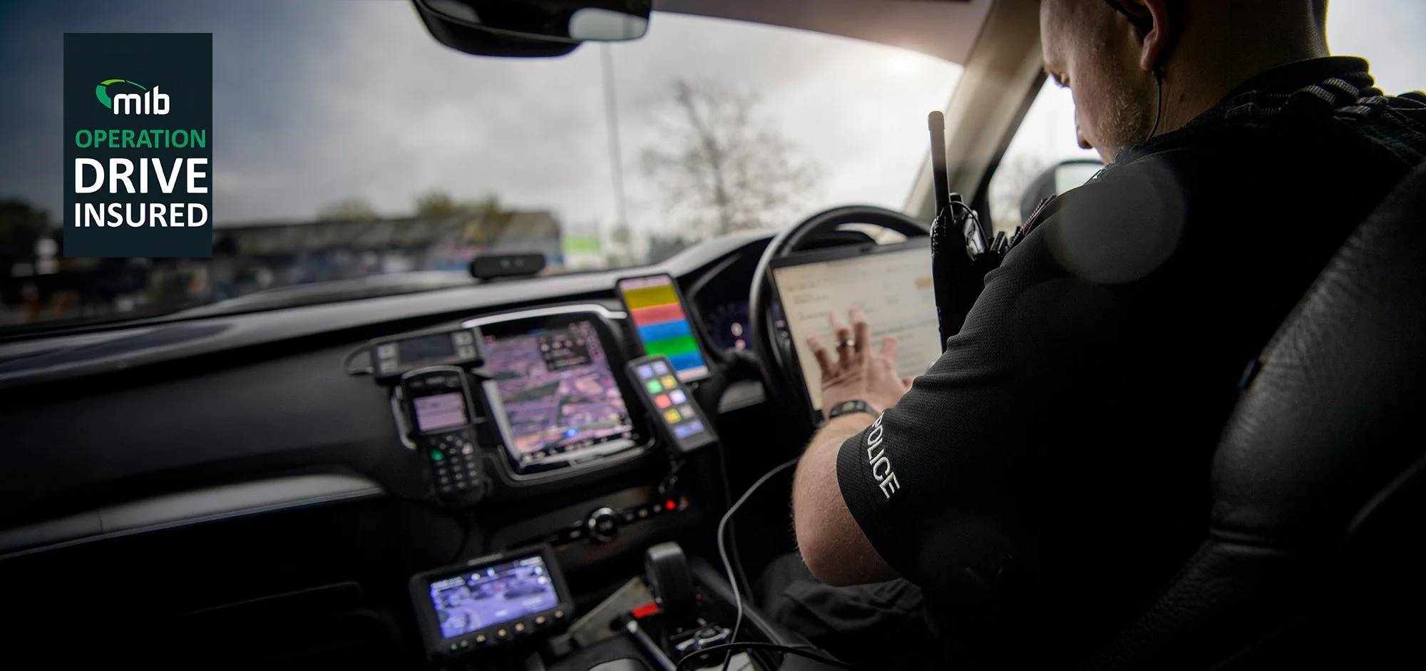 Police man sat in police car using a laptop.