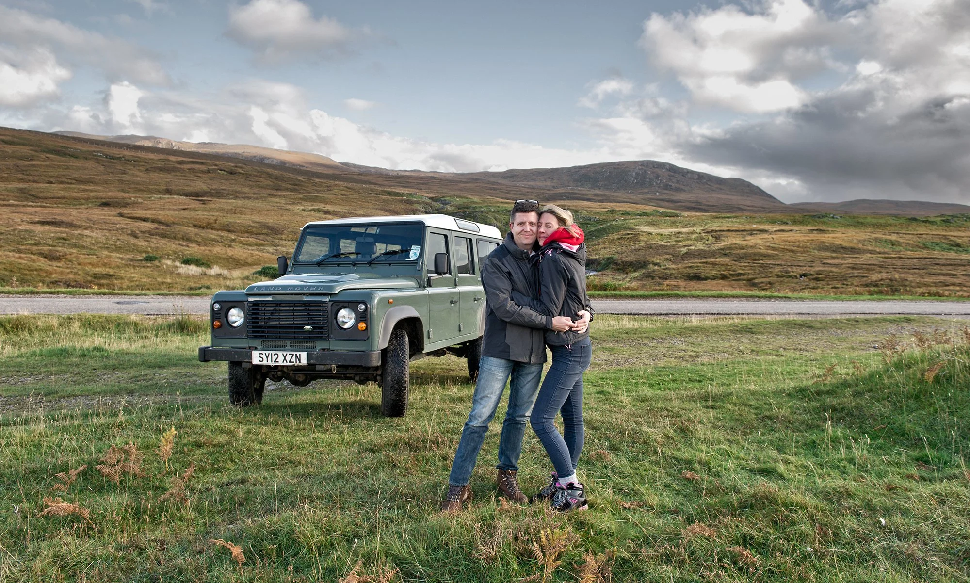 Couple standing in front of old Land Rover Defender