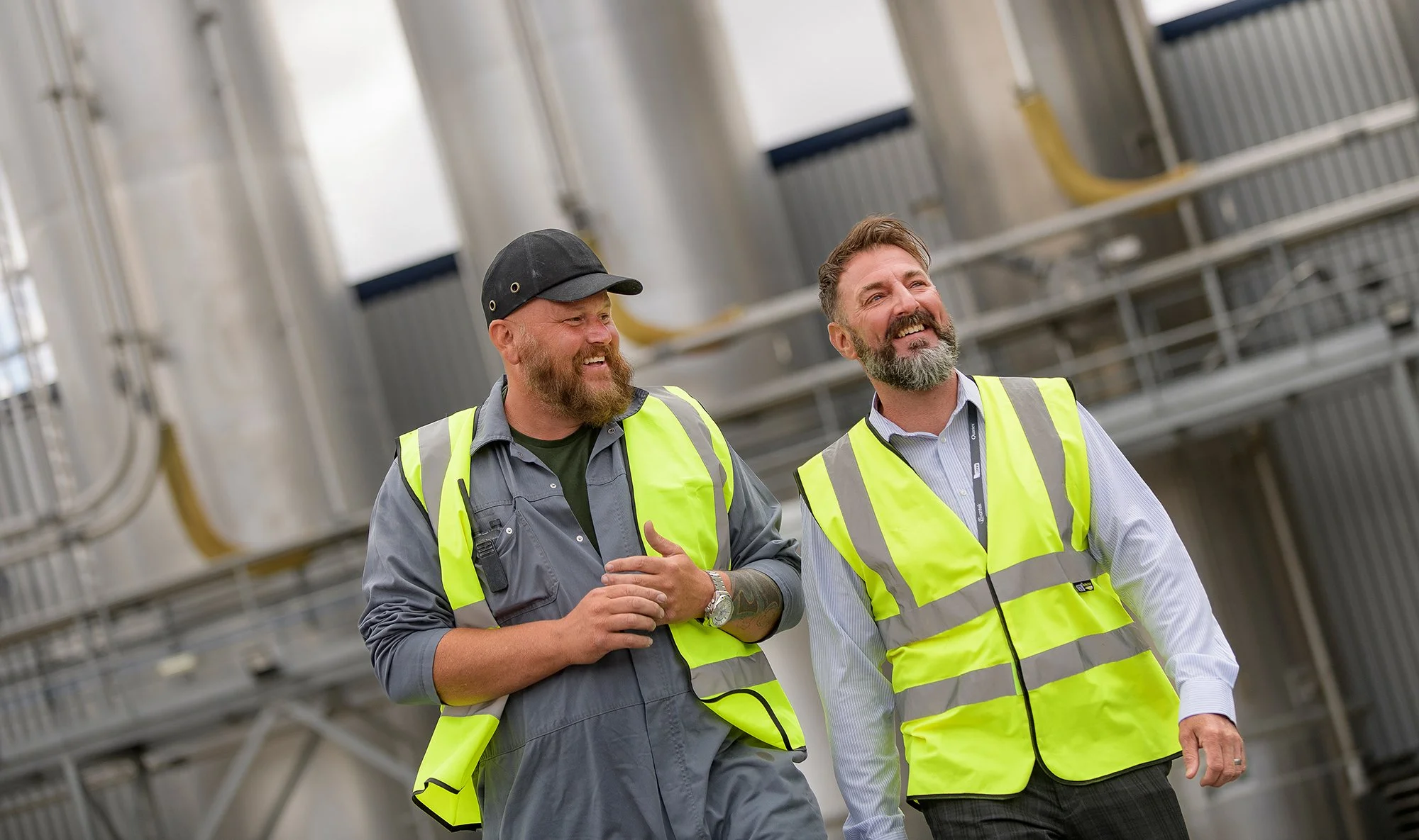 Industrial workmen walking near large storage tanks.