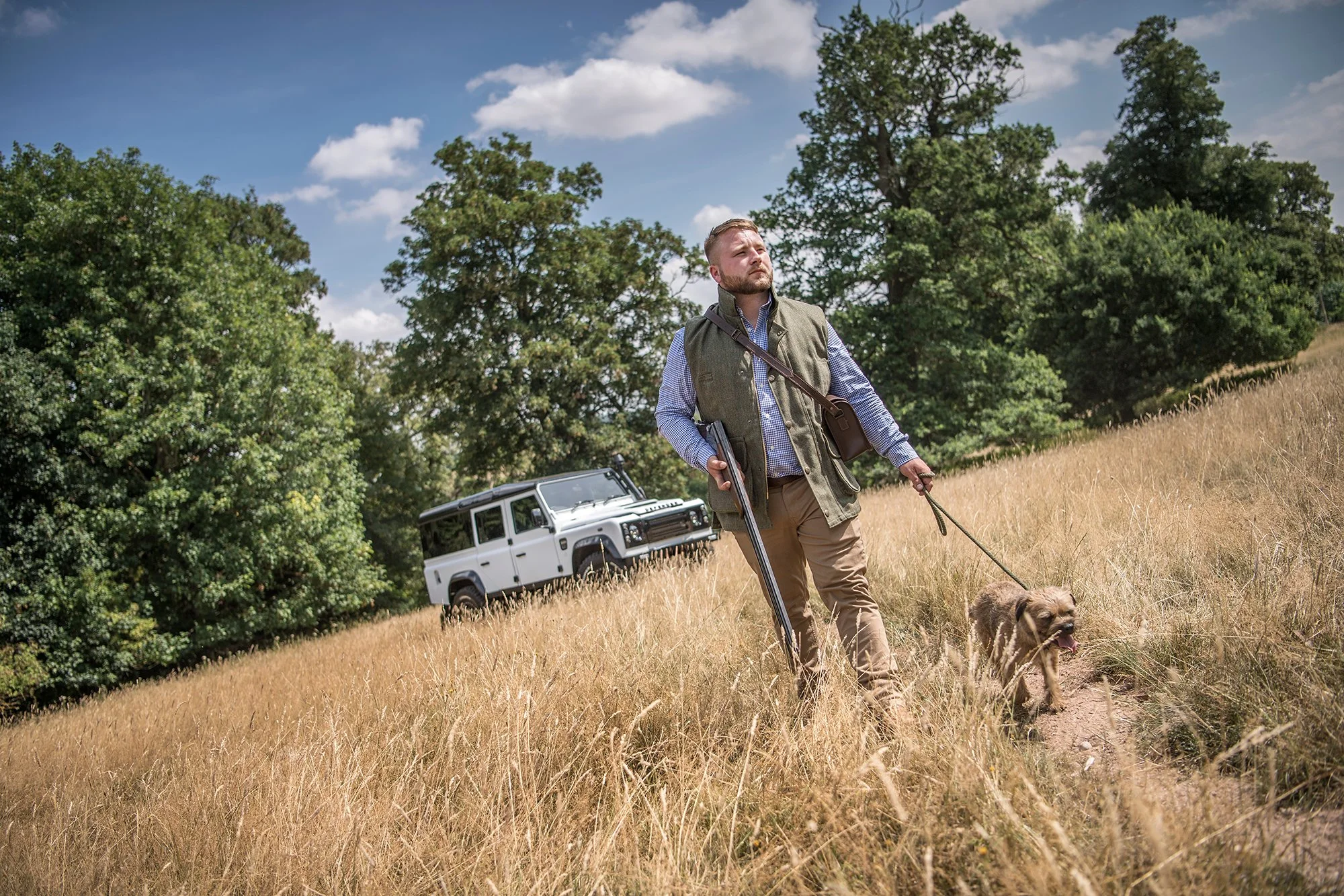 Man walking dog near white Land Rover in field
