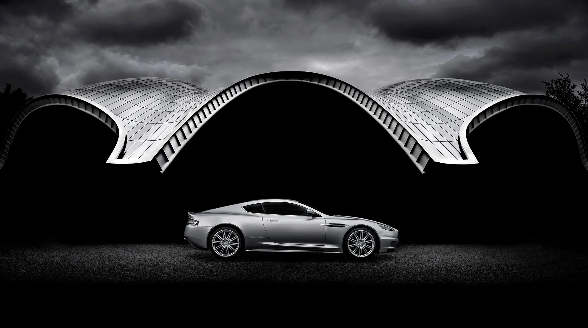 Aston Martin DBS side profile with modern architecture building in the background. 