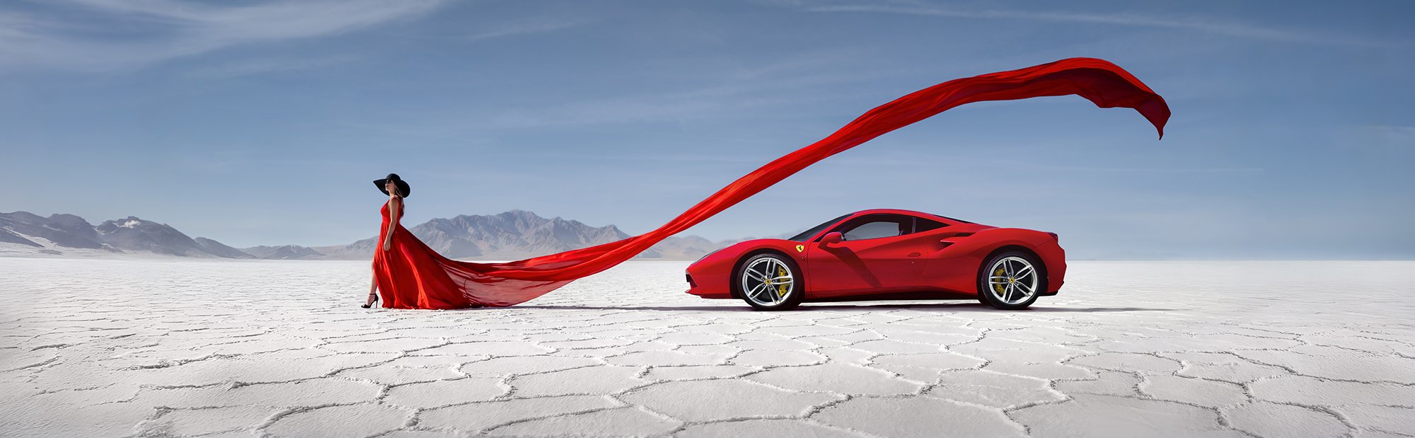 Woman in red dress stood in front of red Ferrari in death valley. 