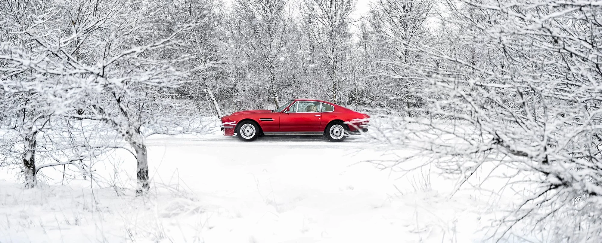 Red Aston Martin V8 Classic car in white snowy scene.