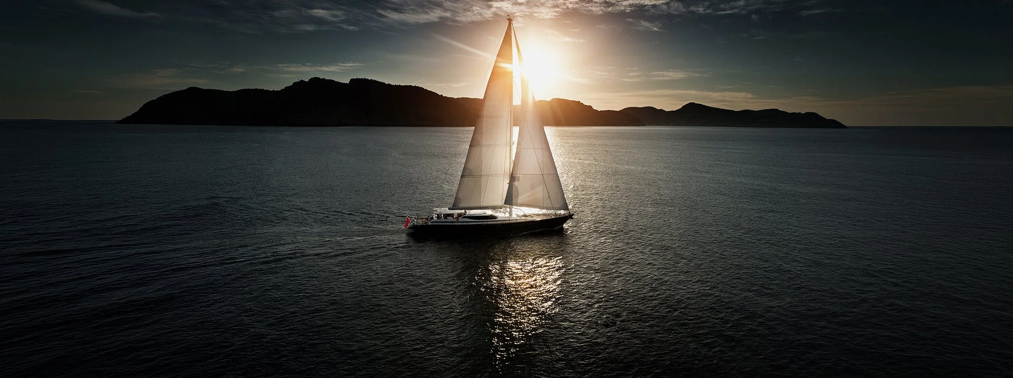Luxury super yacht sailing across open water  with sun rise in the background.
