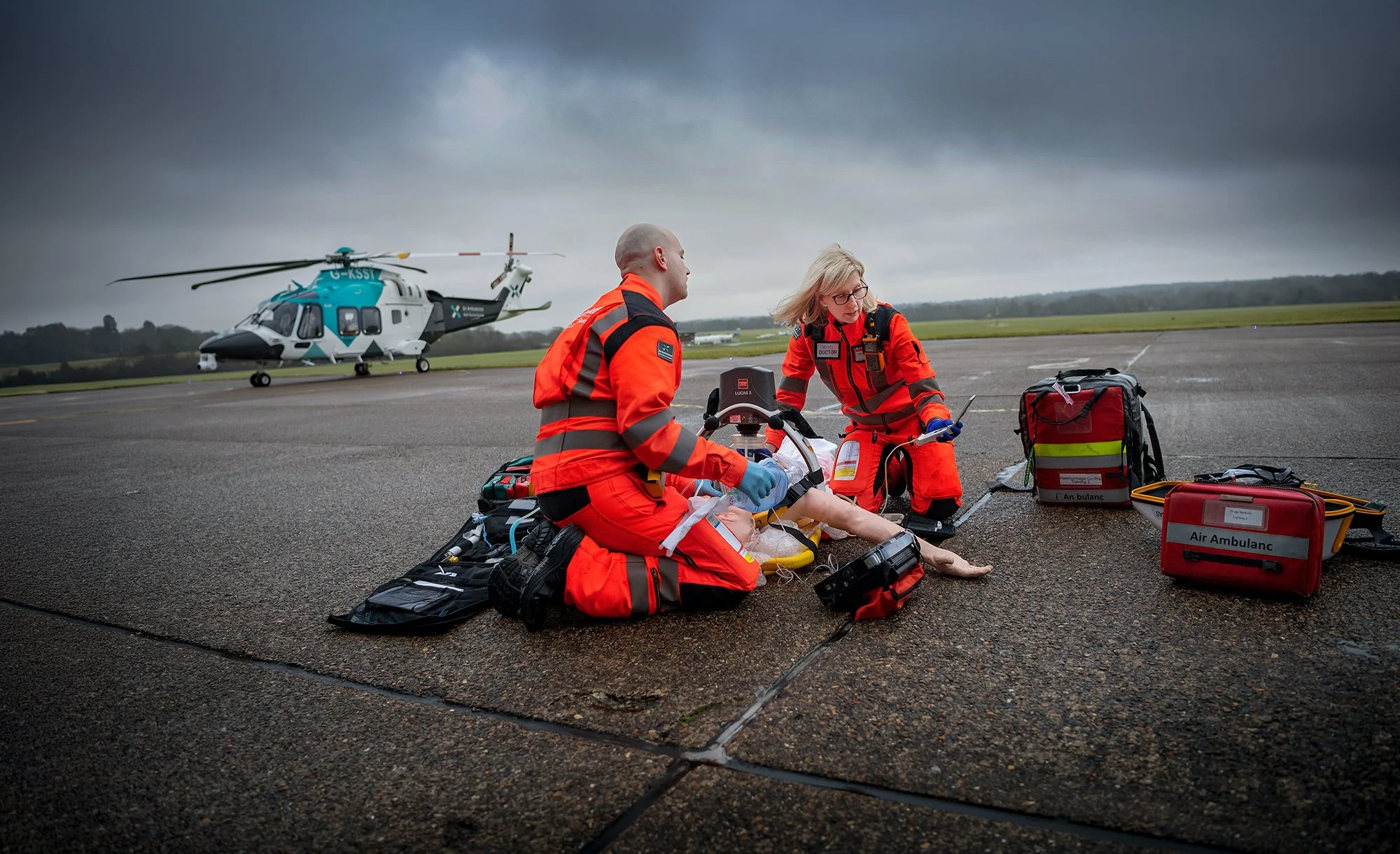 Air ambulance doctor and paramedic helping a man on ground with helicopter in background.