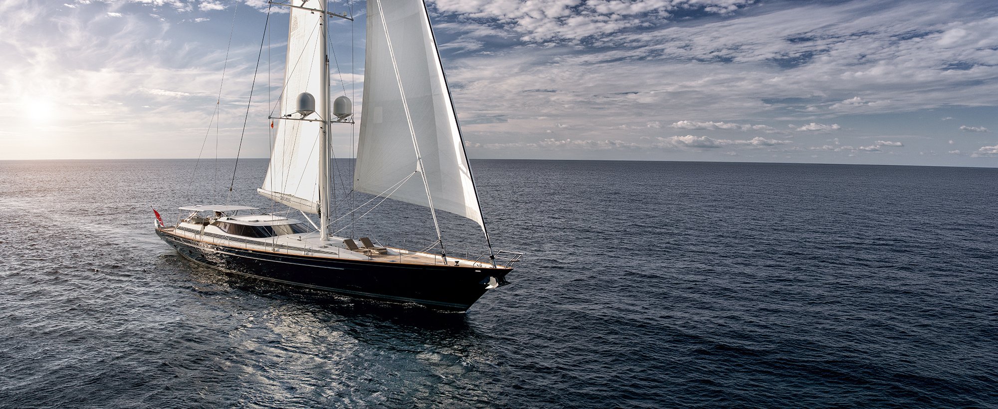 Luxury super yacht sailing across open water  with reflection of sail in water. 