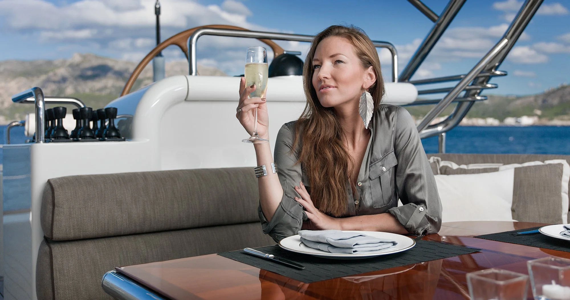 Woman in green dress drinking champagne sitting on deck of luxury yacht.