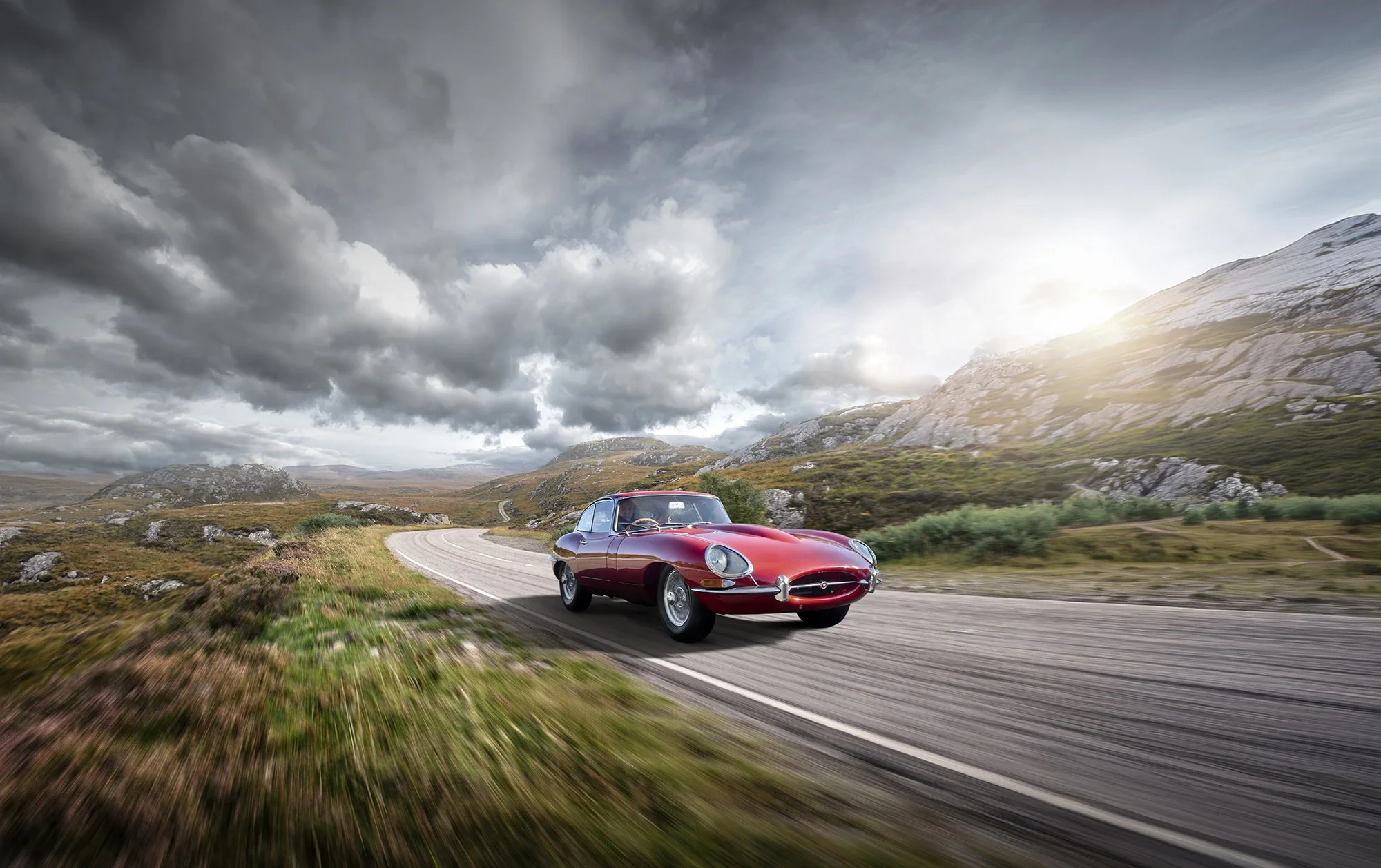 Jaguar E-Type driving on a beautiful country road, car photography.