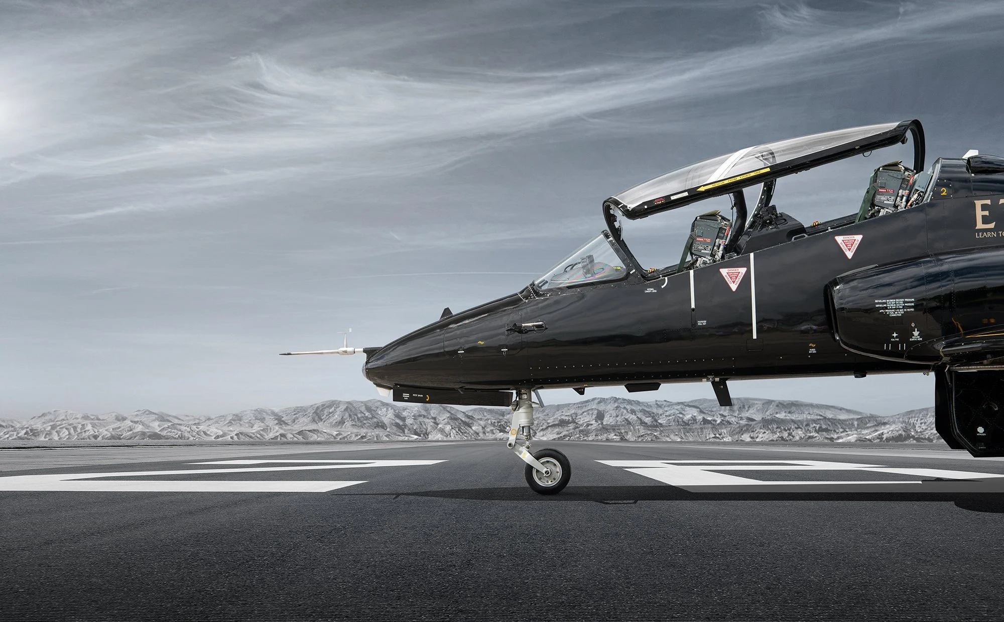 Black fighter jet aircraft on runway with cockpit canopy open.