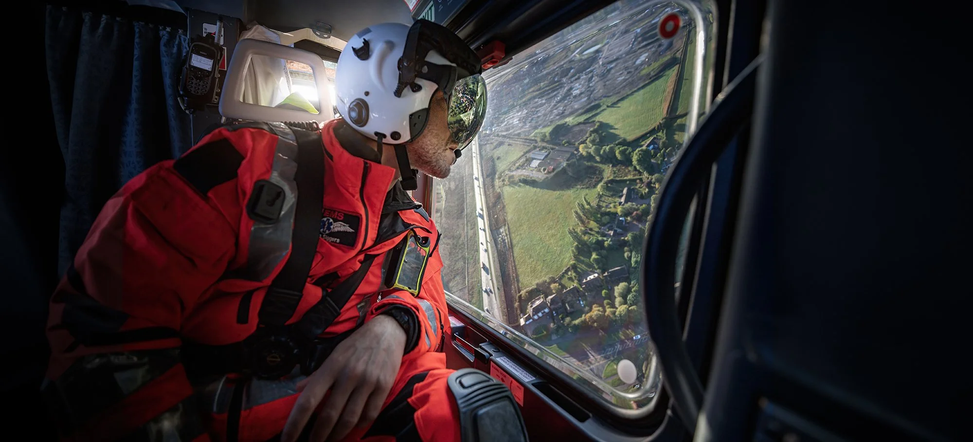 Air Ambulance doctor wearing a helmet looking out of helicopter window at motorway below.