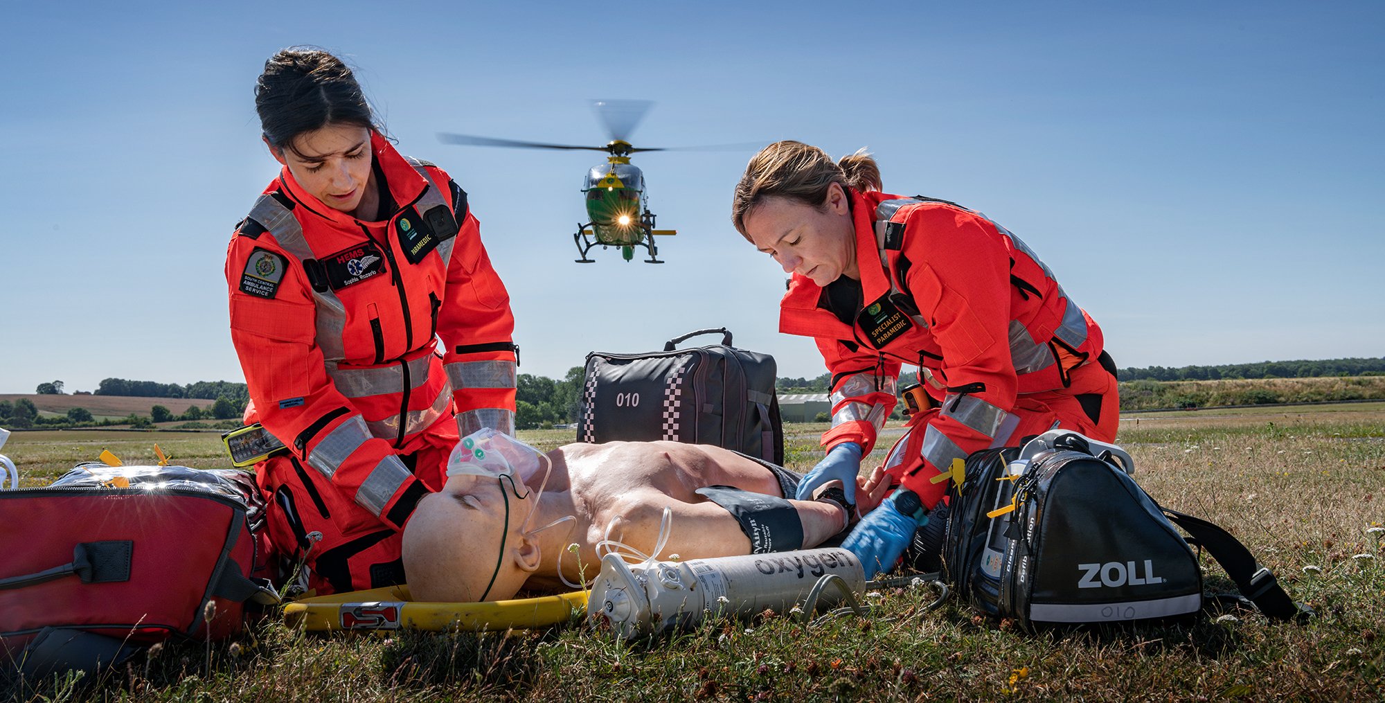 Air ambulance doctor and paramedic helping a man on ground with helicopter hovering in background.