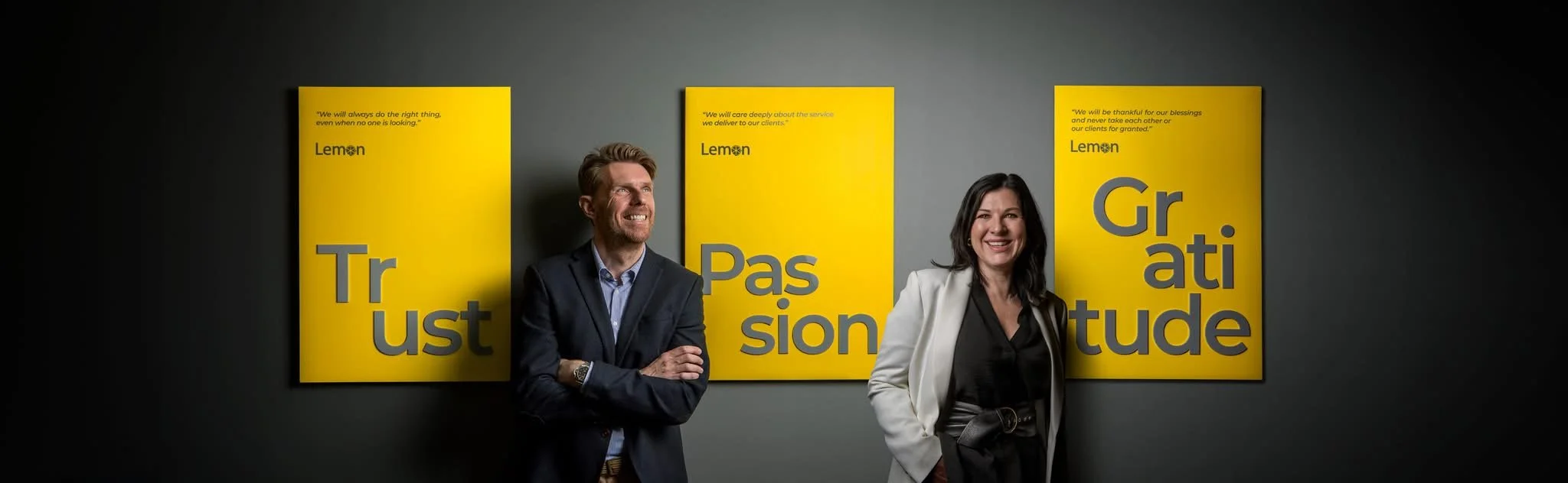 2 people stood in front of 3 yellow wall panels with text on.