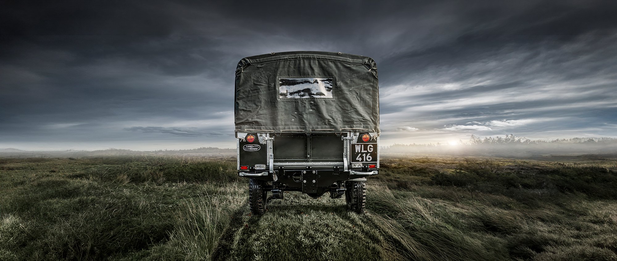 Vintage Land Rover Defender in field, rear view.