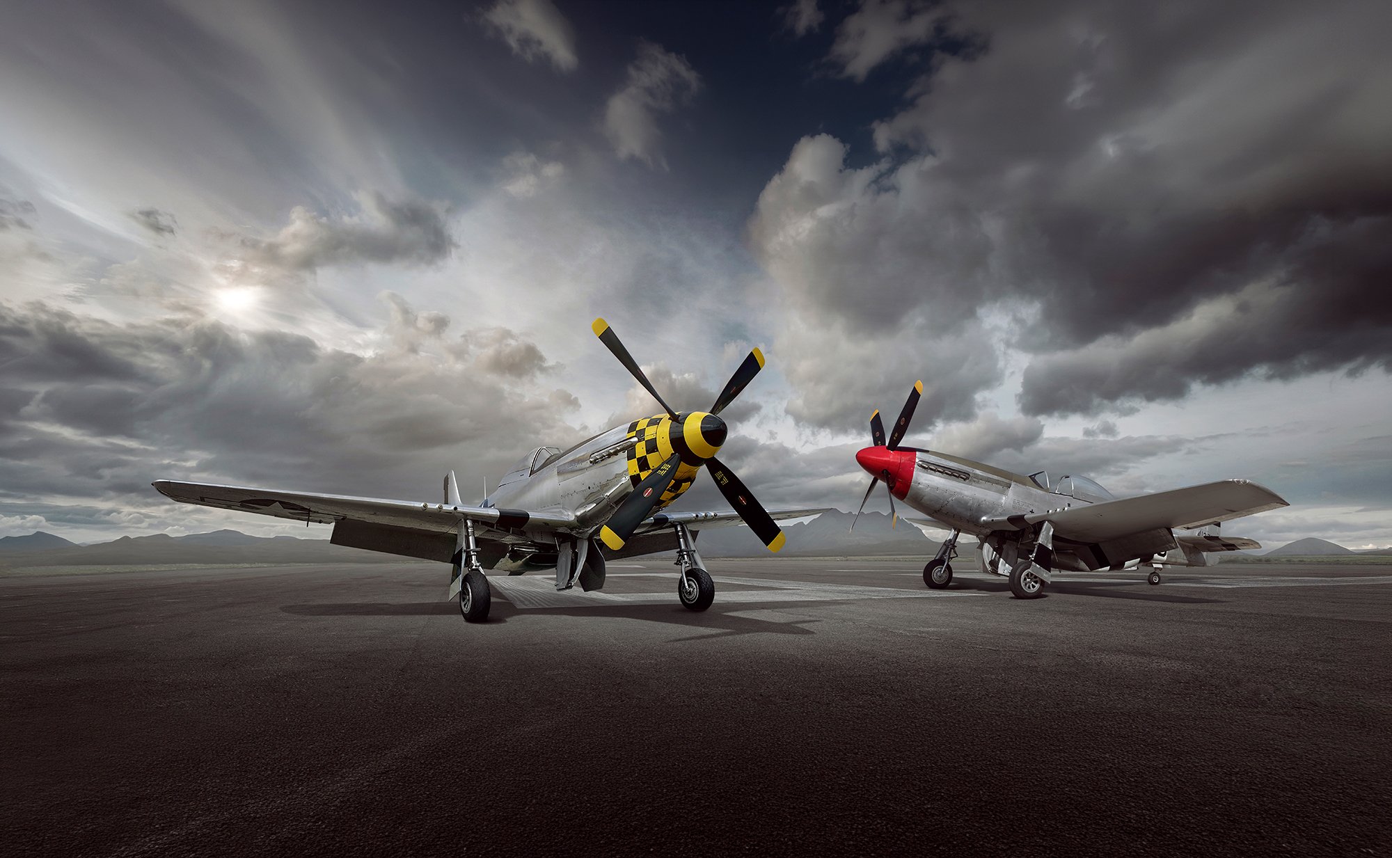 Two P51 Mustang aircraft on a runway with cloudy sky behind. Aviation photographer, Tim Wallace.