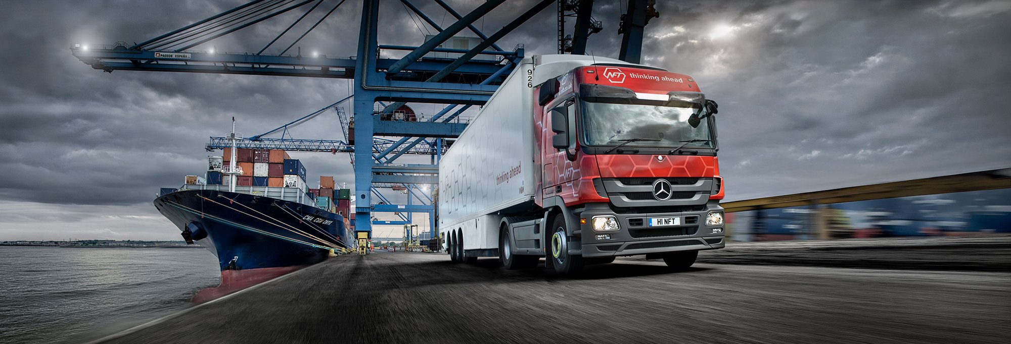 Logistics truck driving at port with ship in background.
