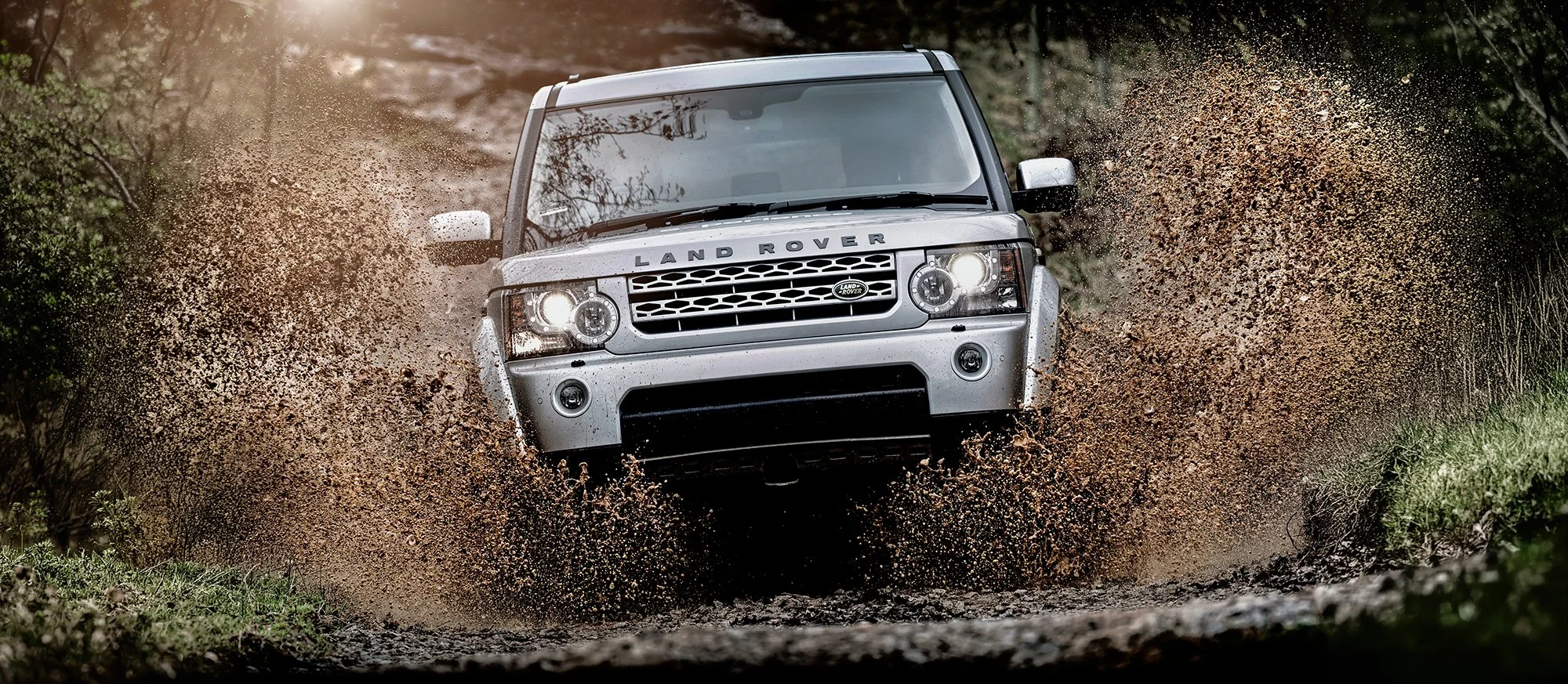Land Rover driving fast through water with big splashes each side.
