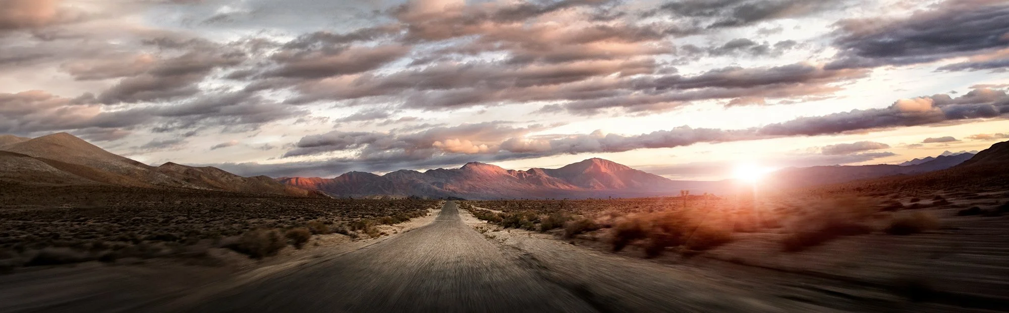 Desert road as the sun is setting with mountains in background.