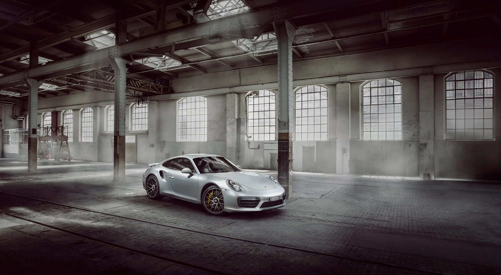 Silver Porsche 911 car inside a old warehouse building with daylight through large windows in background.