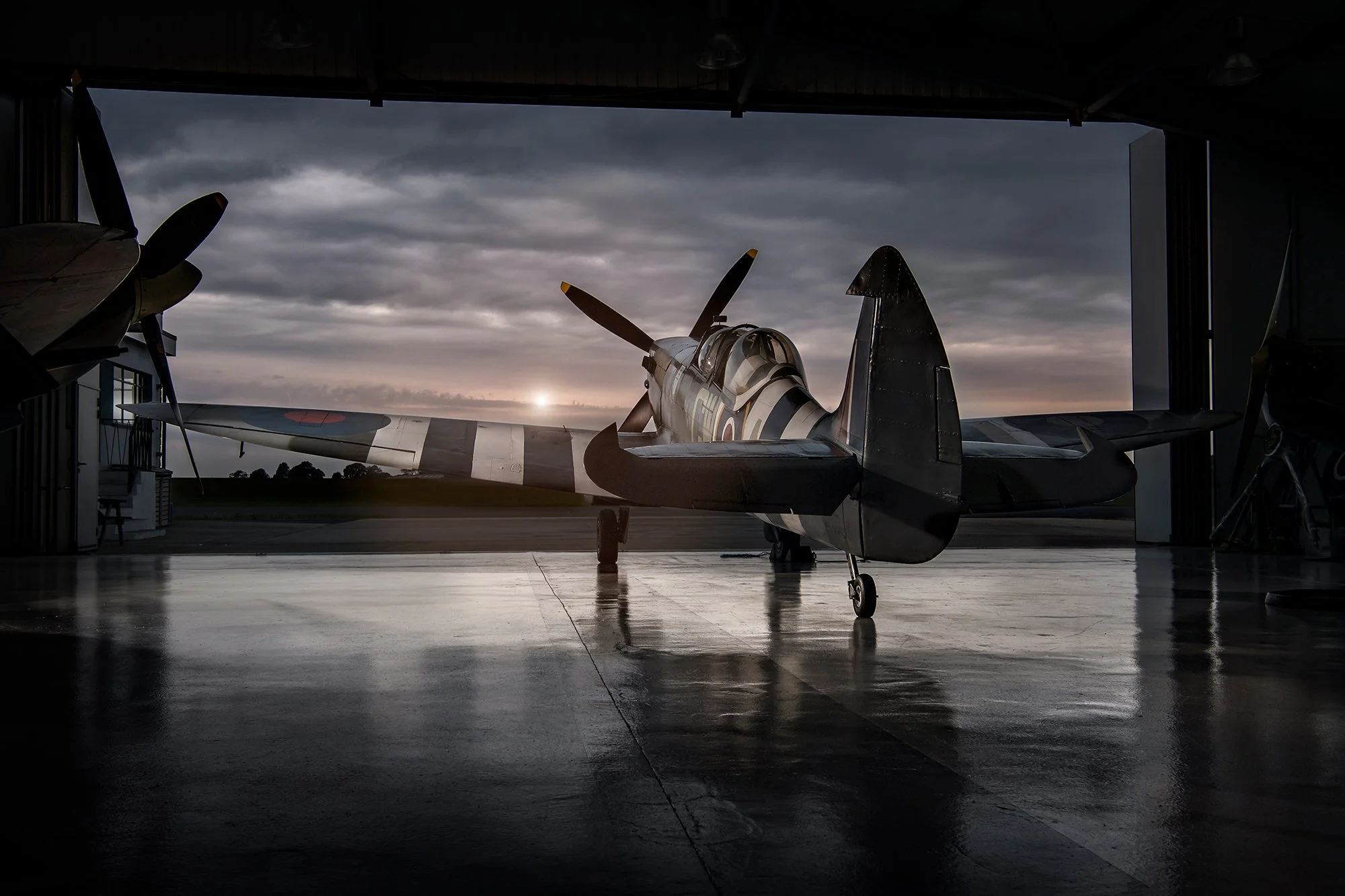 Spitfire aircraft in hanger as sun rises.