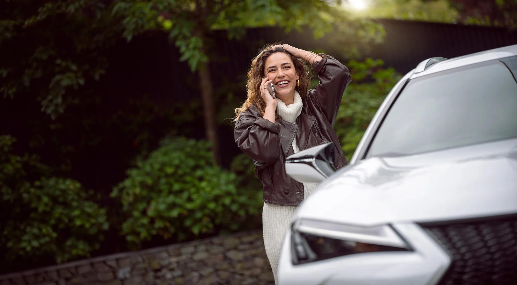 Woman on phone standing near white Lexus car.
