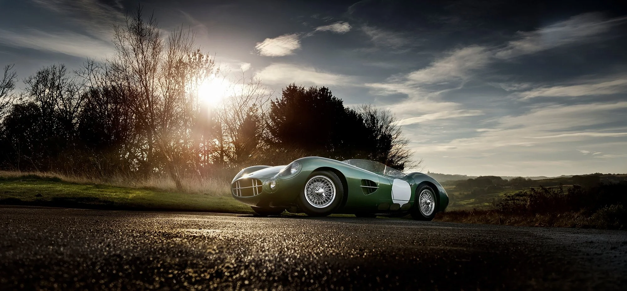 Aston Martin DB1/4 Race car on country road with sun setting in background.