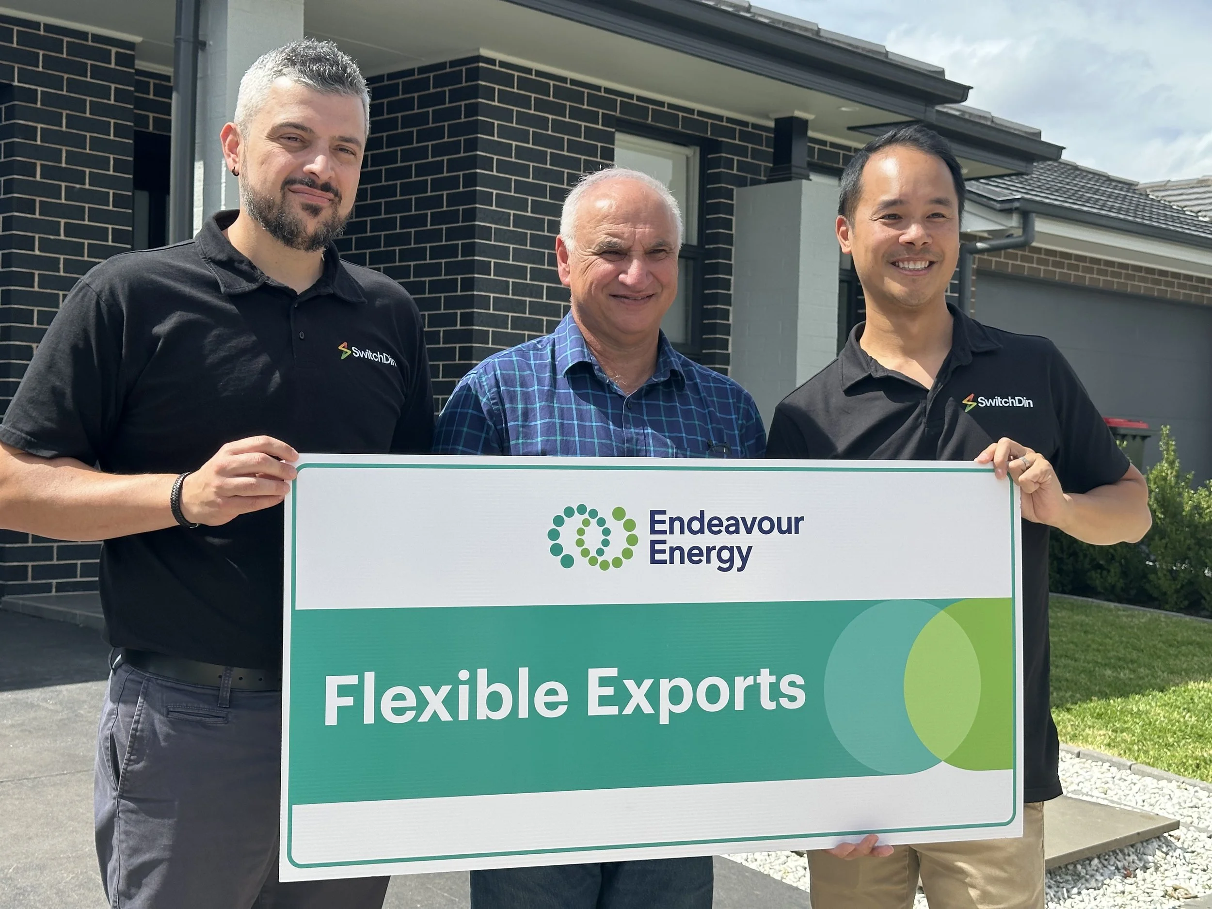 A young man with dark skin and short black hair sitting on a beige padded bench in a simple room, wearing a gray polo shirt and cream-colored pants, with a neutral expression and a shadow cast on the wall.