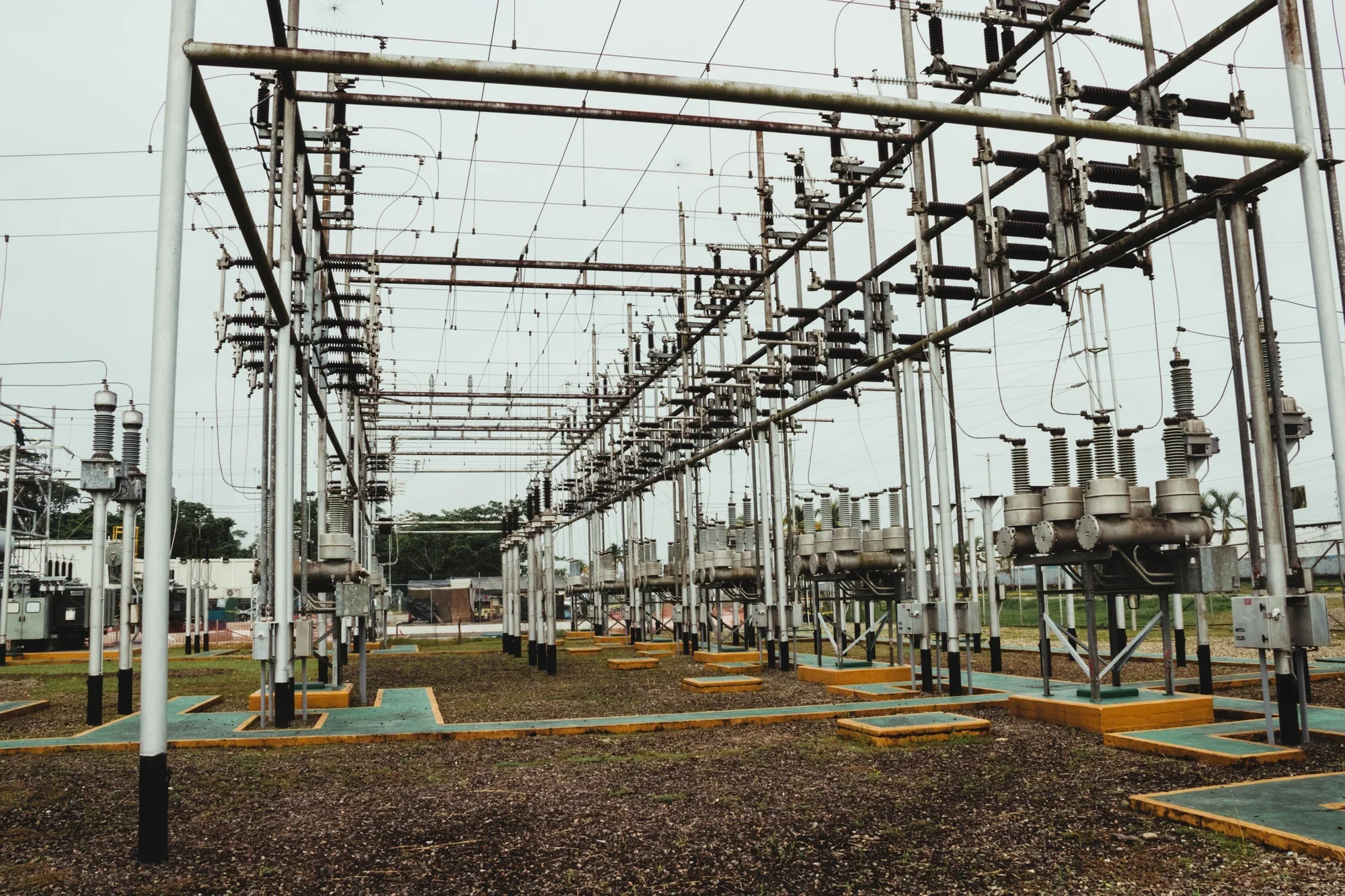 Electrical substation with metal framework, insulators, and transformers, set outdoors on a cloudy day.