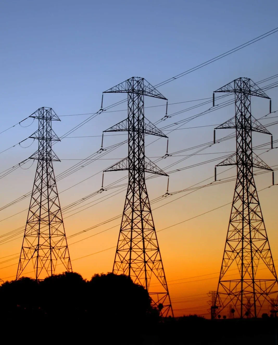 Electricity transmission towers silhouetted against a sunset sky.