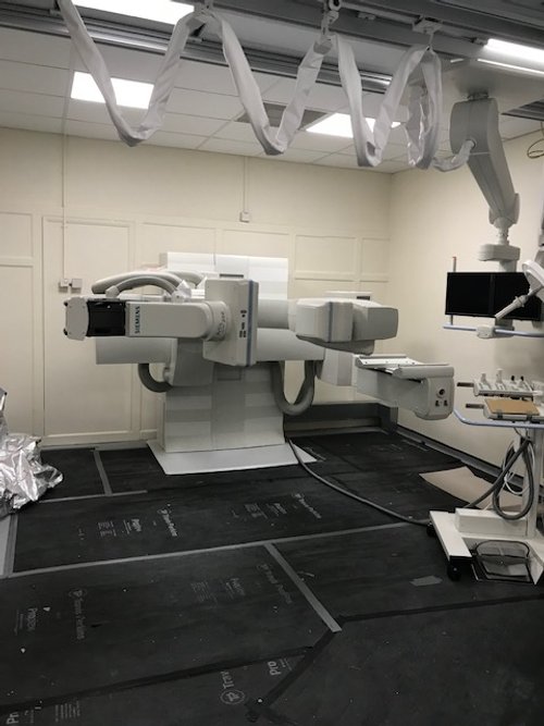 Medical room with an advanced X-ray or imaging machine, hanging white tubes, and a monitor.