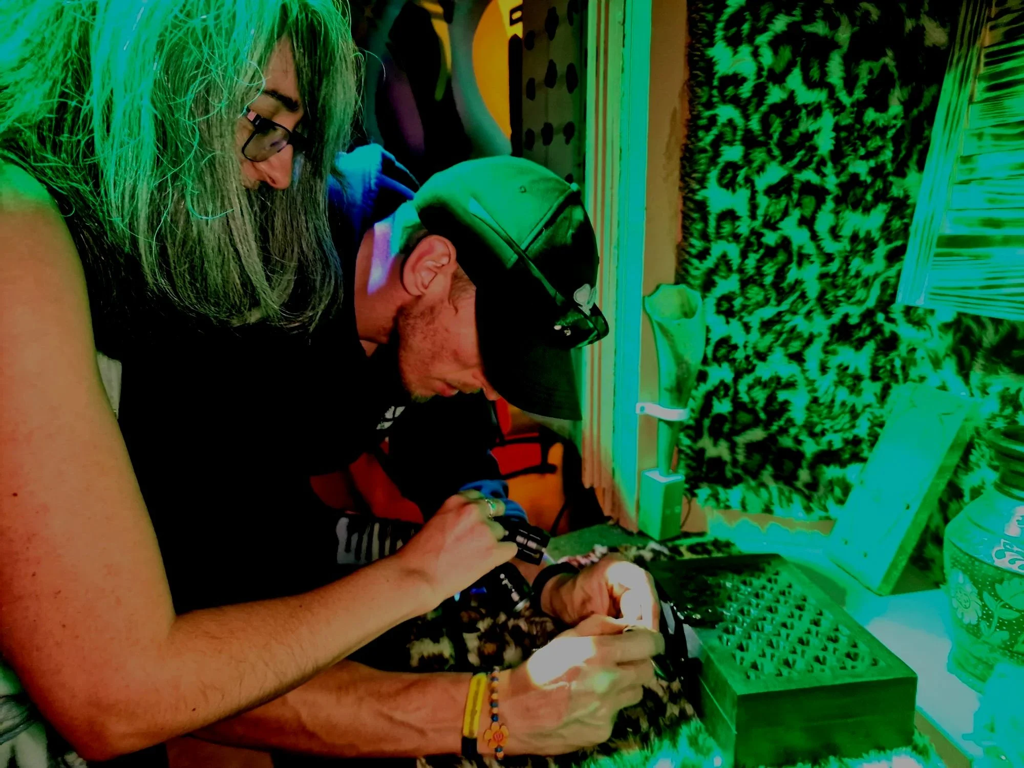 Two people working on a small electronic project at a desk, surrounded by various electronic components, with colorful lighting effects.