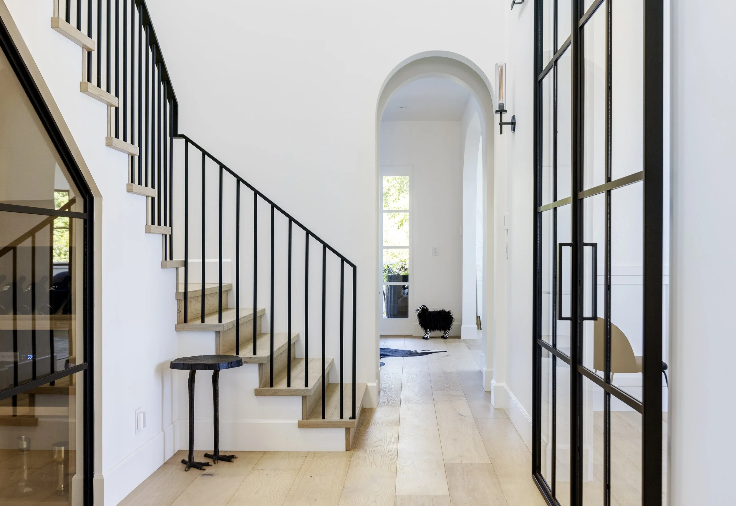Interior photo of The Farm showcasing internal staircase, hallway and arch doorway into living room. Light wood flooring, black steel framed windows