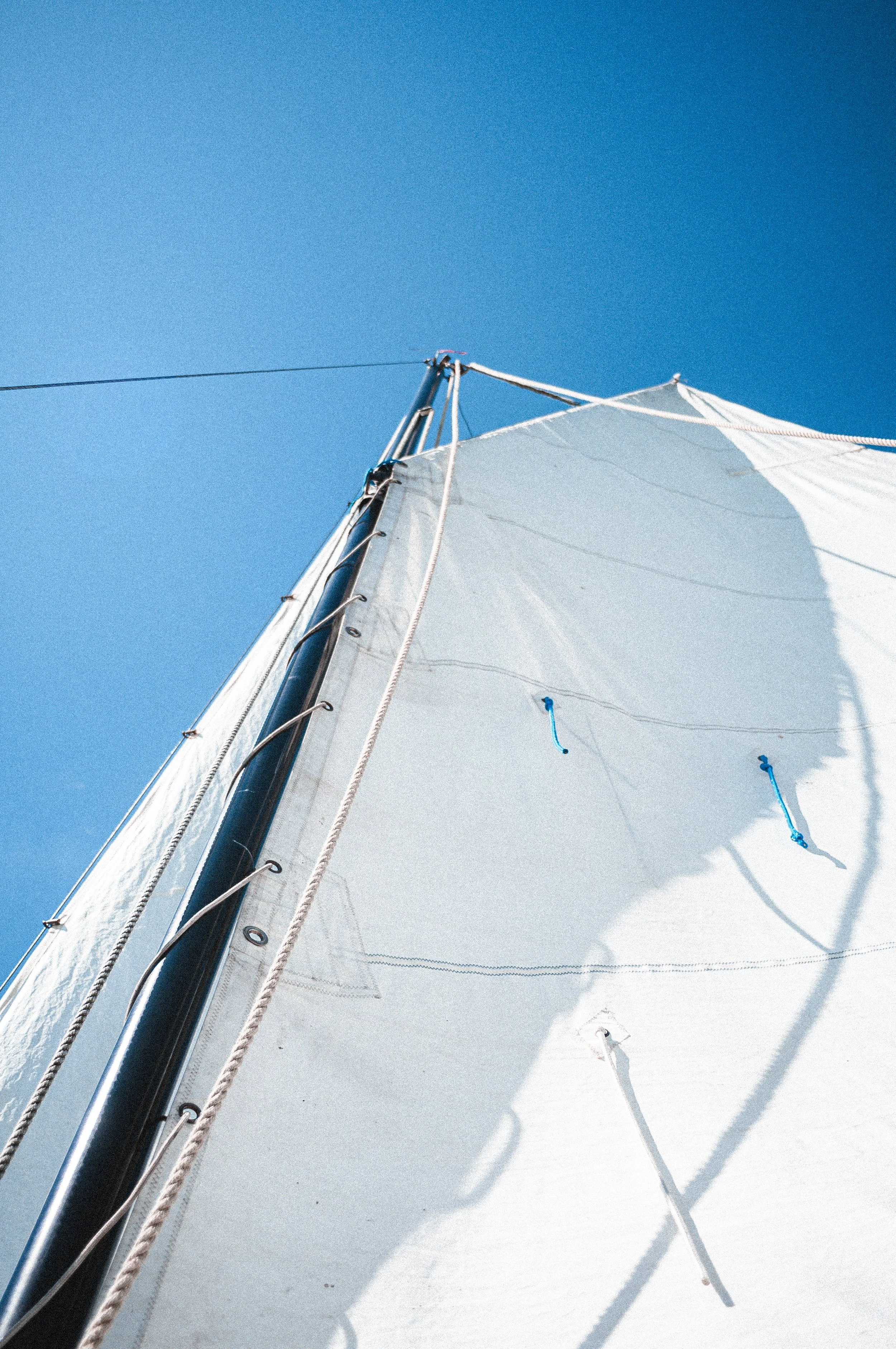 Close-up van de hoge mast van een zeilboot met een witte zeil tegen een heldere blauwe lucht.
