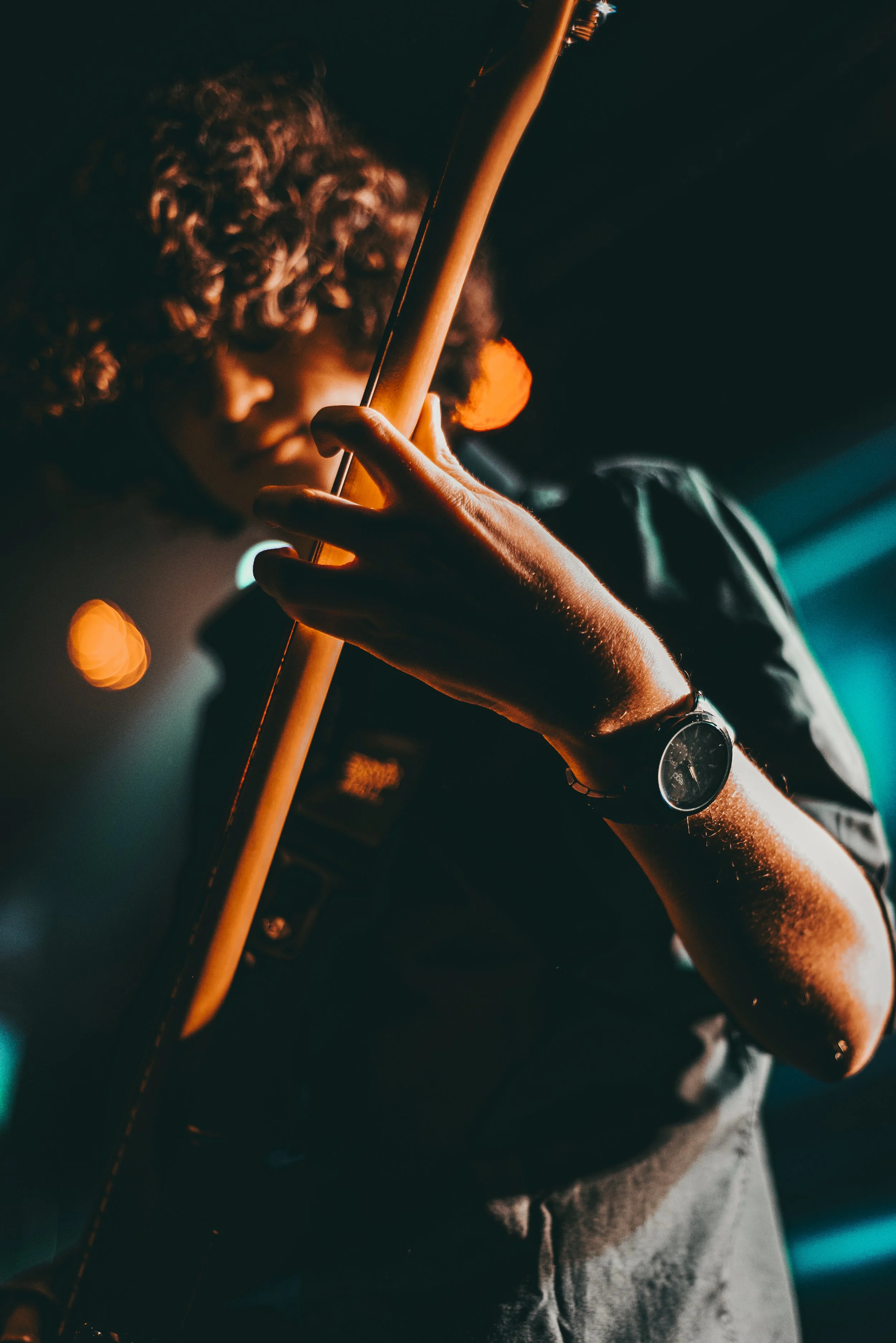 Een persoon met curly haar die viool speelt, met een watch op de pols, in een donkere setting met verlichting.