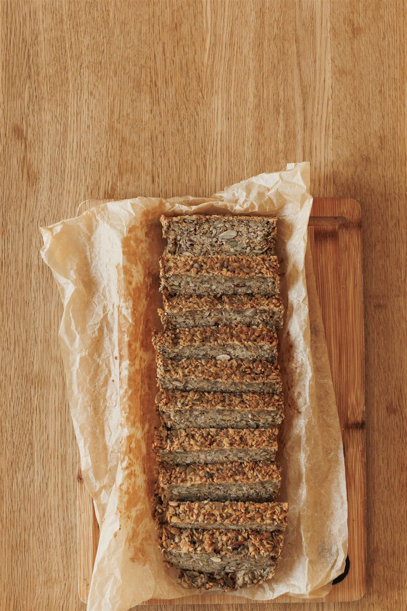 A rustic loaf of gluten free seeded bread, golden brown with a dense, nutty texture, sliced to reveal the mix of oats, seeds, and nuts inside.