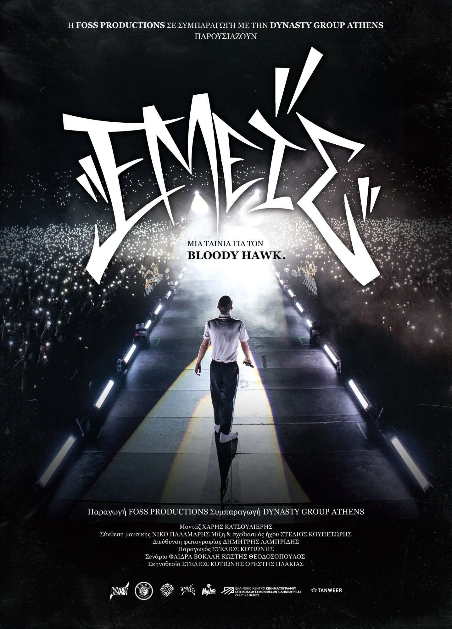 Promotional poster featuring a performer walking on stage with a large crowd holding up lights in the background. The text is in Greek and English, mentioning a movie called 'Bloody Hawk' and production details.