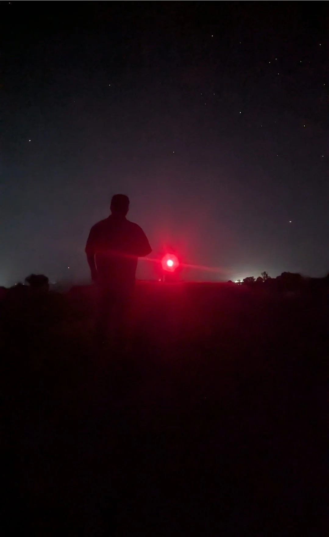 Silhouette of a person standing outdoors at night under a starry sky, with a bright red light source in front of them.