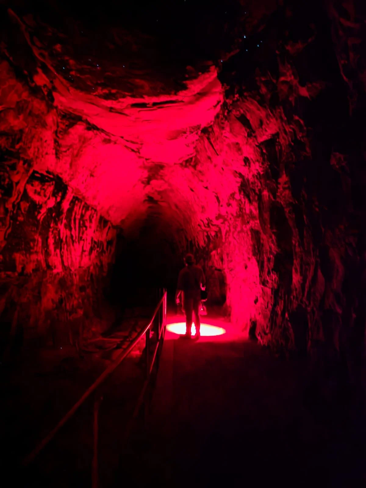 A person standing in a dark, tunnel-like space illuminated by red lights on the rocky walls and ceiling.